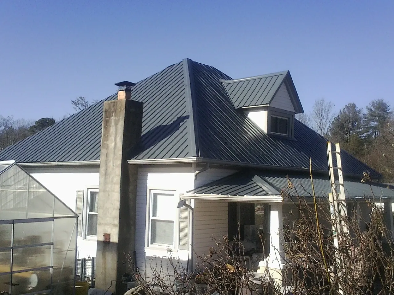 Dark blue standing seam metal roof on a white farmhouse with dormer — Slate & Tile Roof Repair by Roofing Brothers in North Hampton