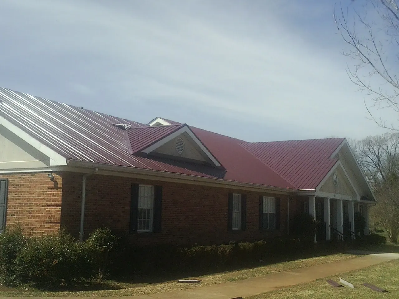 Red metal roof with gabled entries on a long brick building, from a Hail Damage Roof Repair job in North Hampton